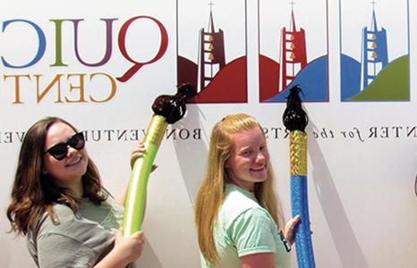 Two Quick Center educators holding giant paint brushes by the traveling Artmobile.